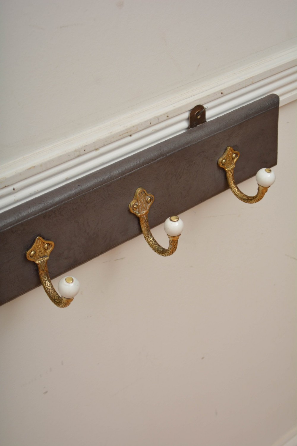 A long dark timber wall-mounted coat rack featuring multiple cast brass hooks with white ceramic finials. View V