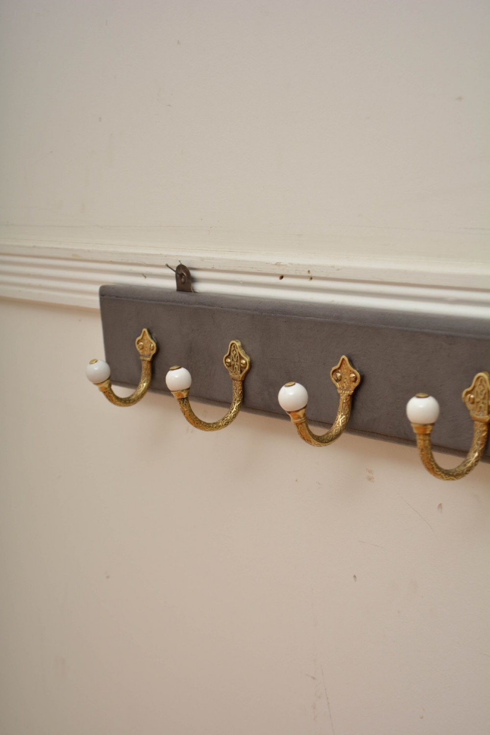 A long dark timber wall-mounted coat rack featuring multiple cast brass hooks with white ceramic finials. View VIII