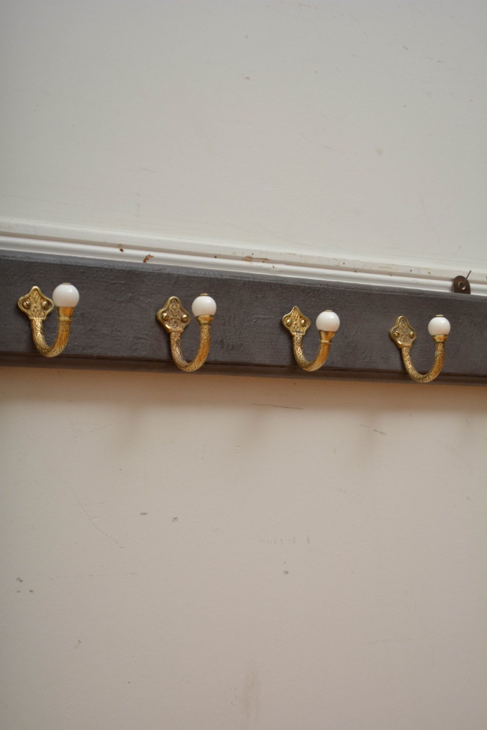 A long dark timber wall-mounted coat rack featuring multiple cast brass hooks with white ceramic finials. View XI