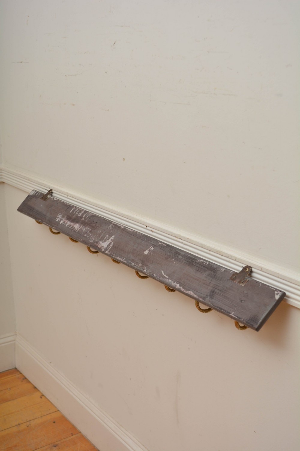 A long dark timber wall-mounted coat rack featuring multiple cast brass hooks with white ceramic finials. View XIII