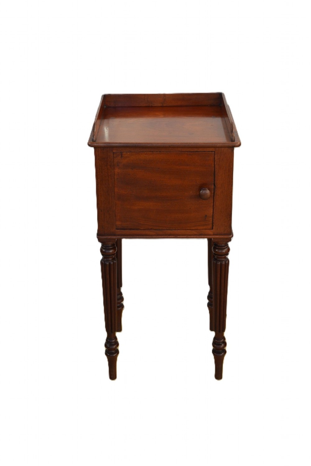 A dark mahogany bedside cabinet featuring a three-sided gallery top, a single door with a turned wooden knob, and four slender reeded legs. View VI