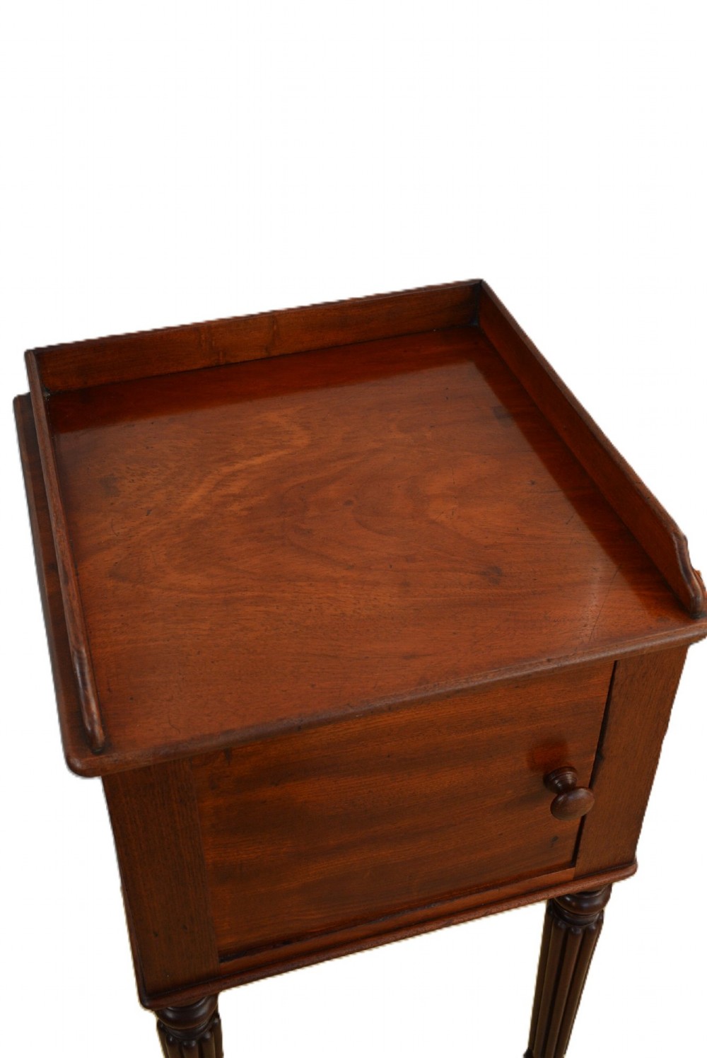 A dark mahogany bedside cabinet featuring a three-sided gallery top, a single door with a turned wooden knob, and four slender reeded legs. View VII