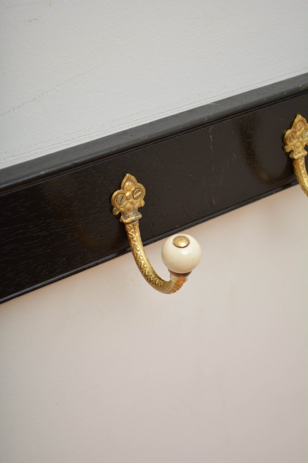 An ebonised black timber rail mounted with four cast brass coat hooks topped with round cream ceramic tips. View III
