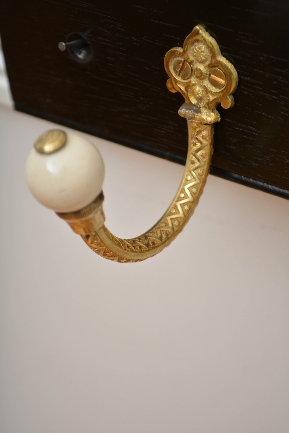 An ebonised black timber rail mounted with four cast brass coat hooks topped with round cream ceramic tips. View VII