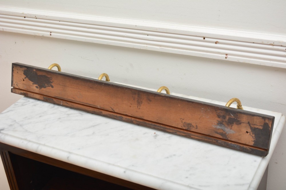An ebonised black timber rail mounted with four cast brass coat hooks topped with round cream ceramic tips. View IX