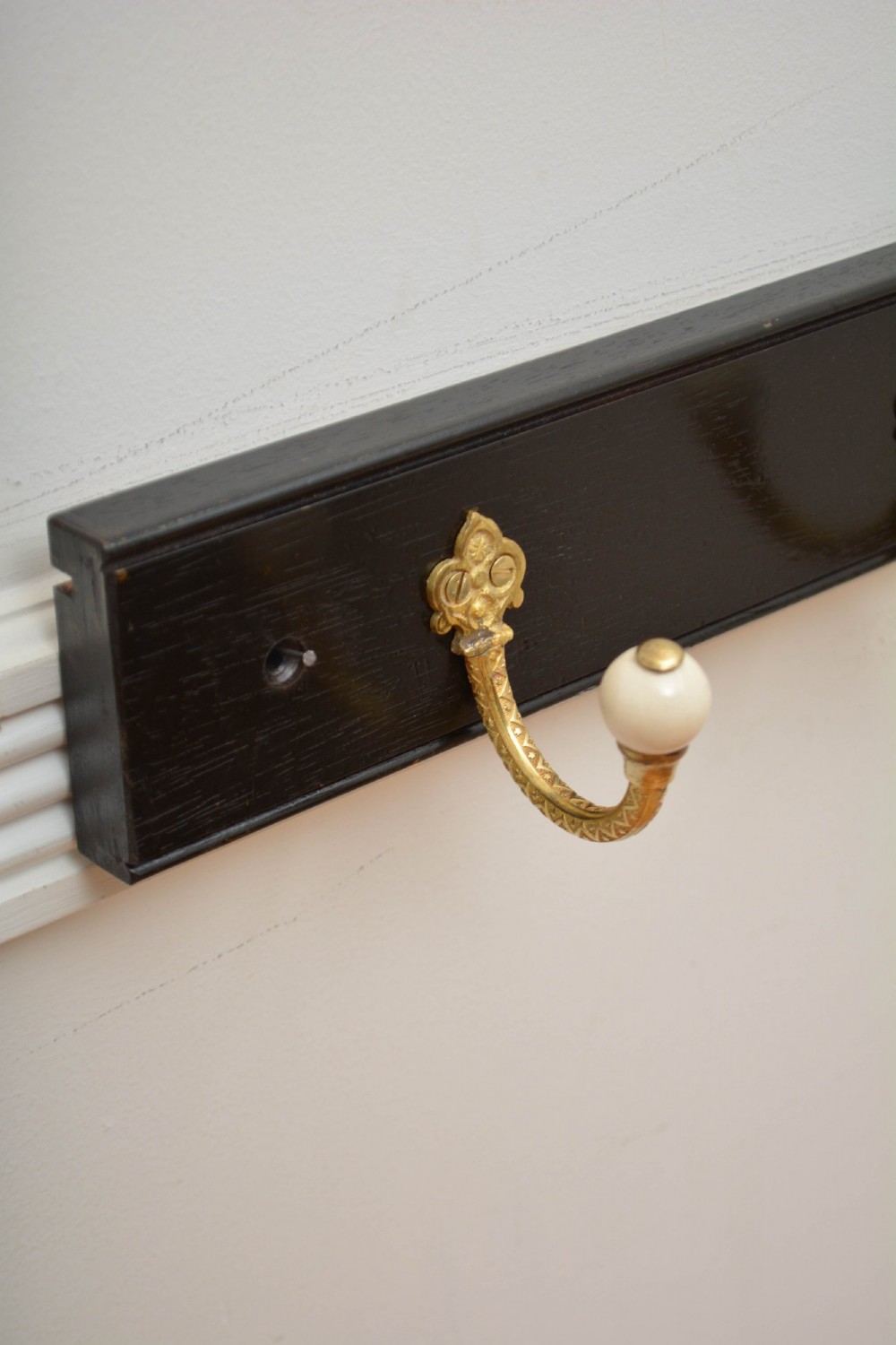 An ebonised black timber rail mounted with four cast brass coat hooks topped with round cream ceramic tips. View XI
