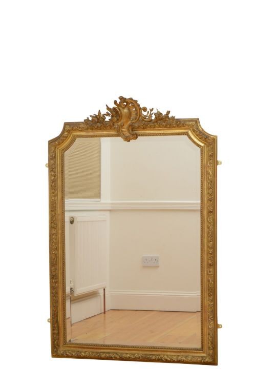 A tall antique giltwood wall mirror featuring an ornate carved floral cresting at the top, decorative foliate moulding along the frame, and original glass. View II