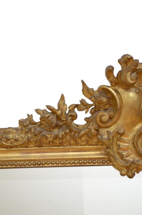 A tall antique giltwood wall mirror featuring an ornate carved floral cresting at the top, decorative foliate moulding along the frame, and original glass. View III