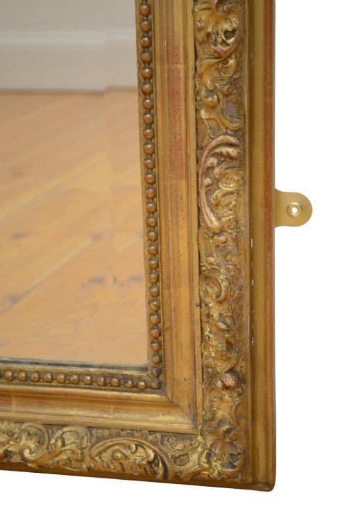 A tall antique giltwood wall mirror featuring an ornate carved floral cresting at the top, decorative foliate moulding along the frame, and original glass. View IV