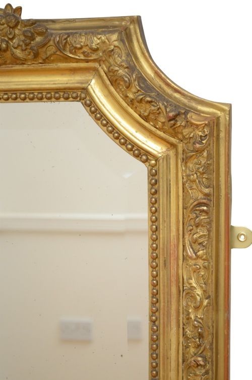 A tall antique giltwood wall mirror featuring an ornate carved floral cresting at the top, decorative foliate moulding along the frame, and original glass. View VIII