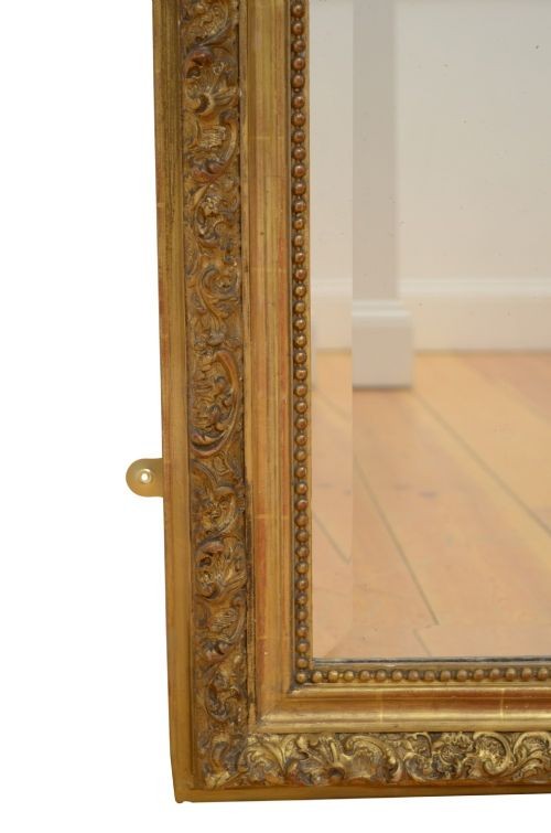 A tall antique giltwood wall mirror featuring an ornate carved floral cresting at the top, decorative foliate moulding along the frame, and original glass. View XII