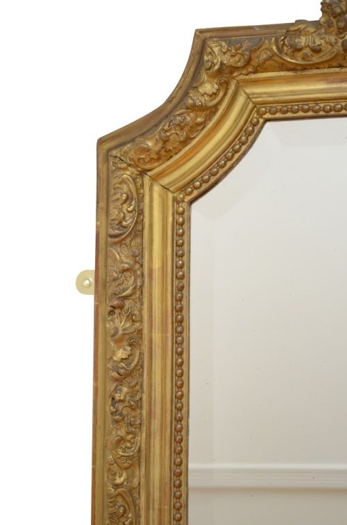 A tall antique giltwood wall mirror featuring an ornate carved floral cresting at the top, decorative foliate moulding along the frame, and original glass. View XIV