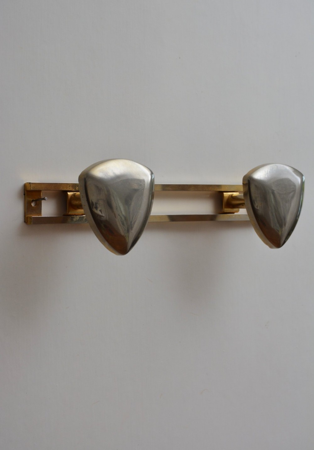 A set of two silver shield-shaped coat hooks mounted on a horizontal gold-toned metal wall bar.