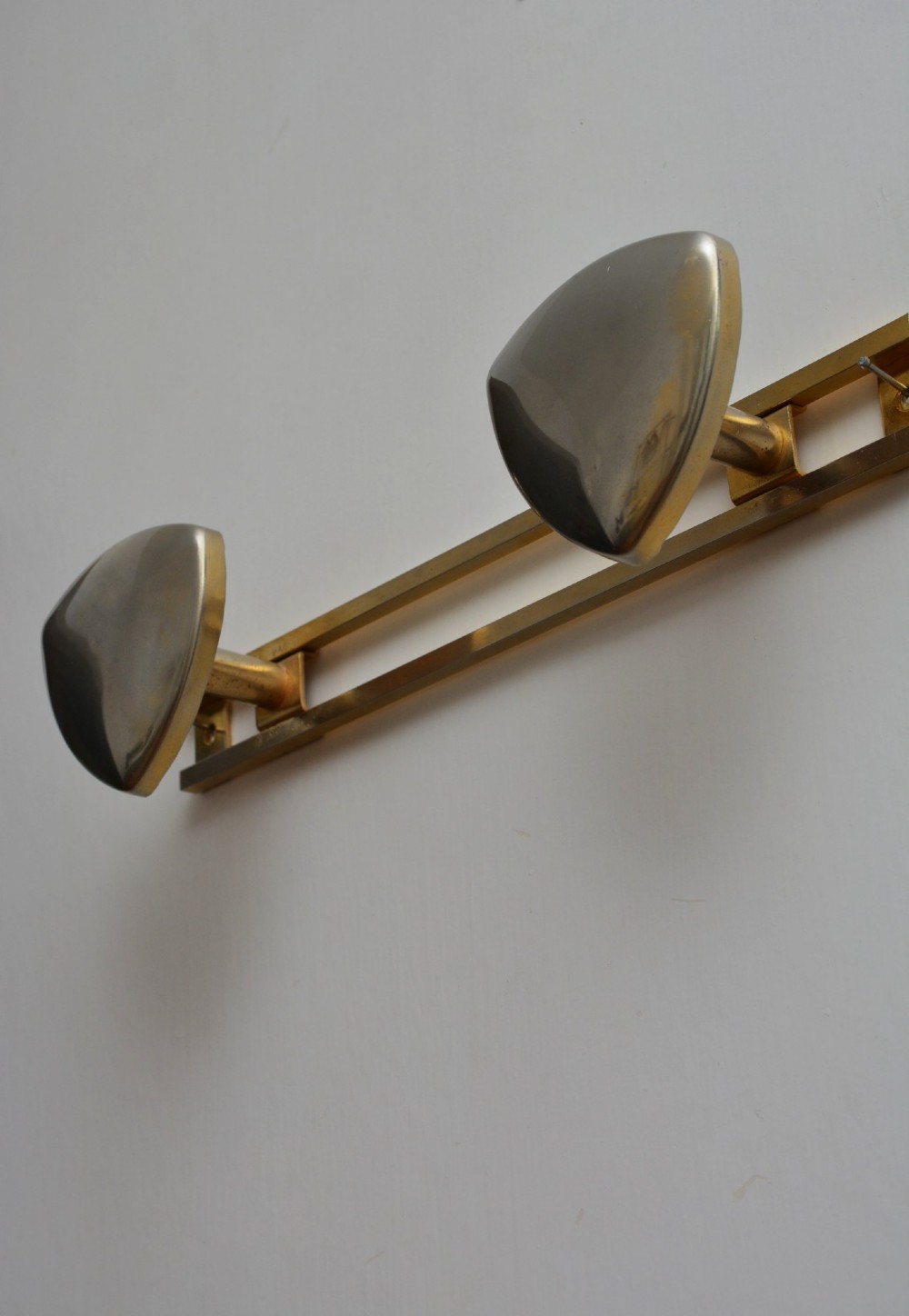 A set of two silver shield-shaped coat hooks mounted on a horizontal gold-toned metal wall bar. View V