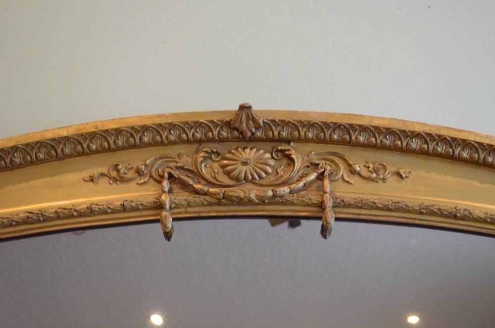 A large arched giltwood overmantel mirror featuring decorative floral moulding and side scroll details. View V