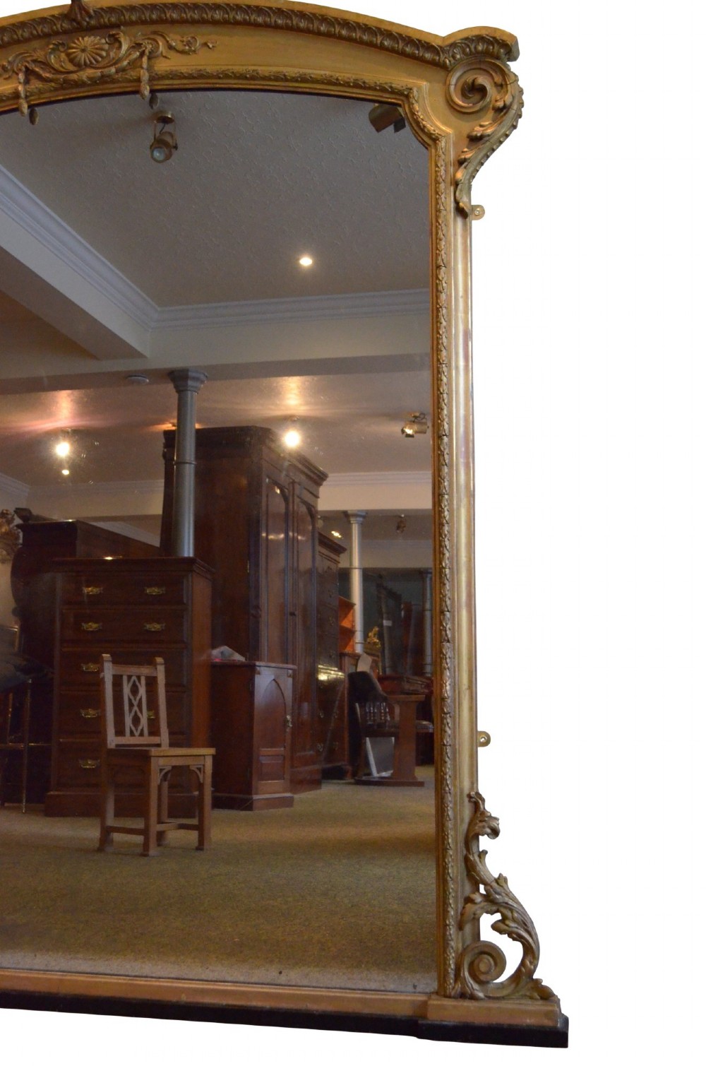 A large arched giltwood overmantel mirror featuring decorative floral moulding and side scroll details. View IX