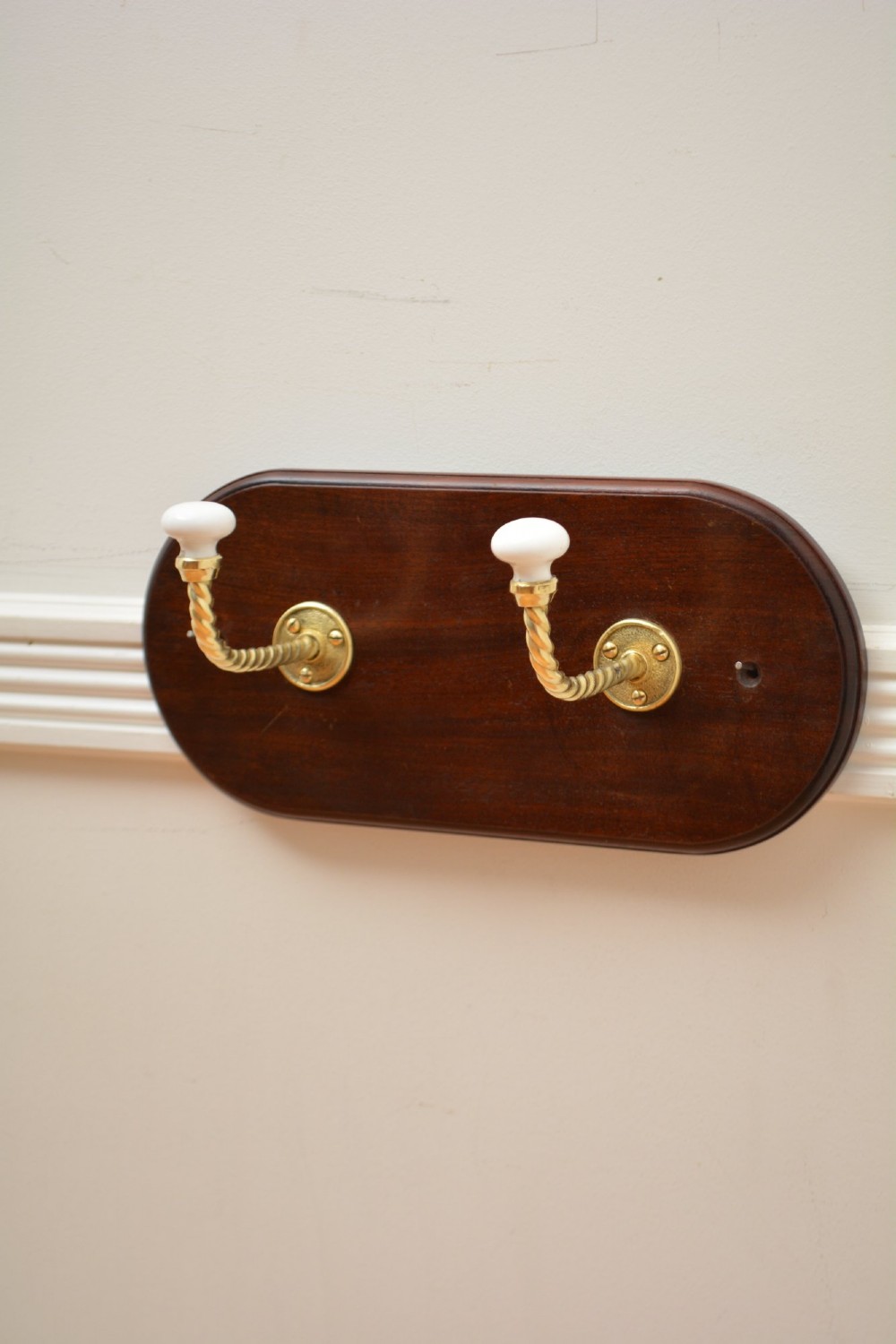 An oval mahogany wood backboard mounted with two twisted brass coat hooks featuring white ceramic end knobs. View III