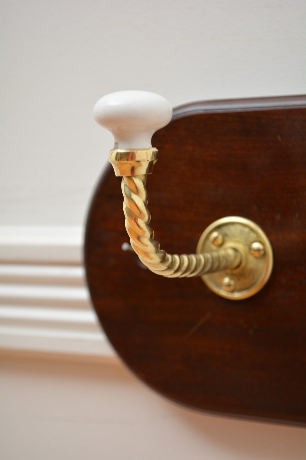 An oval mahogany wood backboard mounted with two twisted brass coat hooks featuring white ceramic end knobs. View V