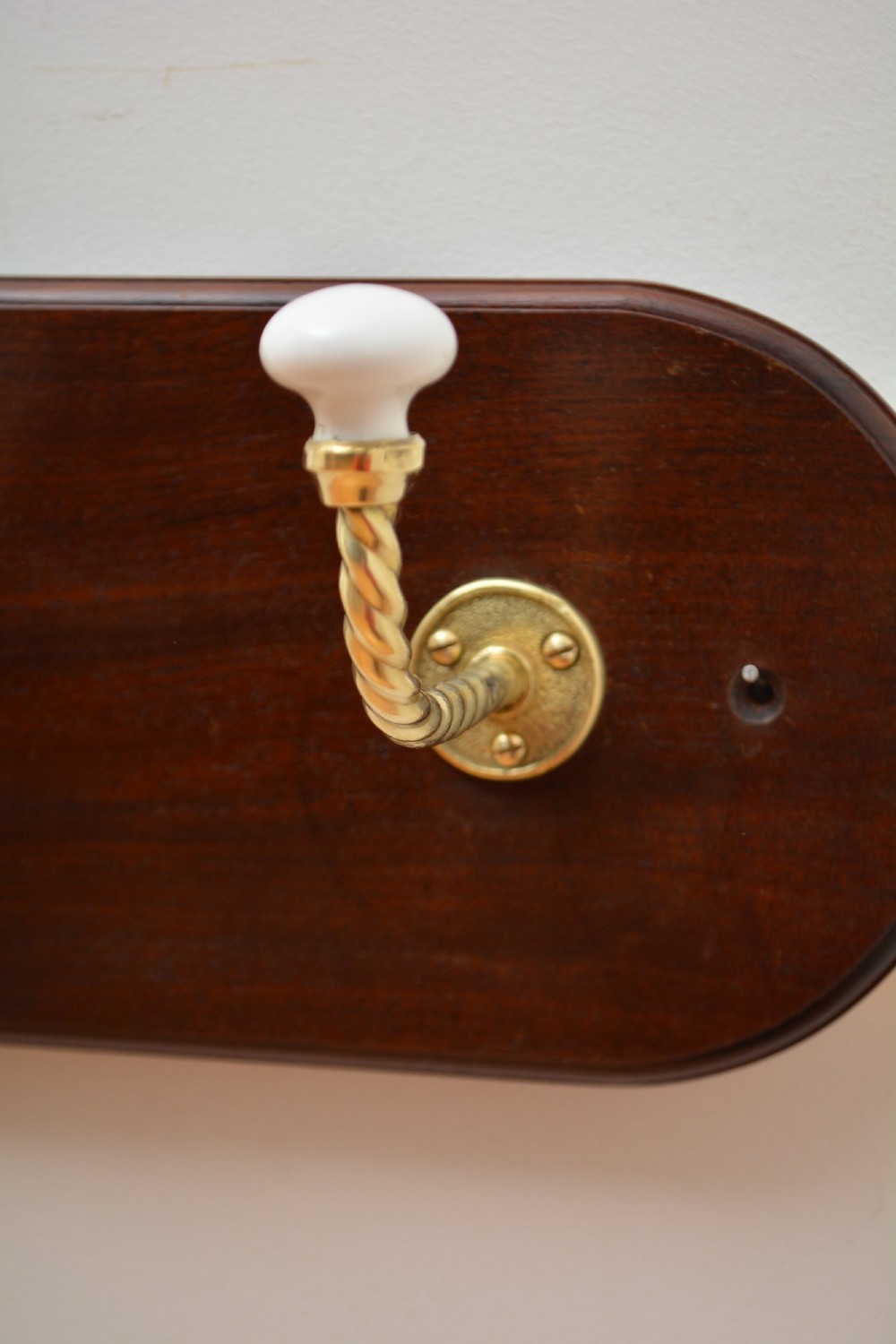 An oval mahogany wood backboard mounted with two twisted brass coat hooks featuring white ceramic end knobs. View VI