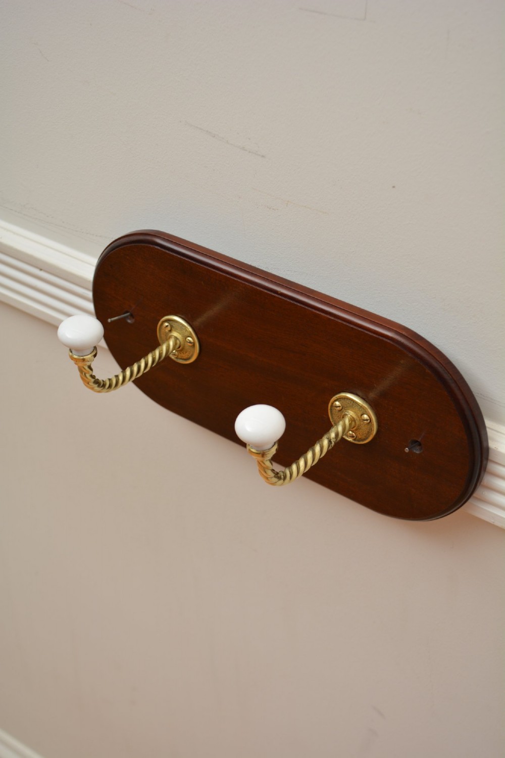 An oval mahogany wood backboard mounted with two twisted brass coat hooks featuring white ceramic end knobs. View VII