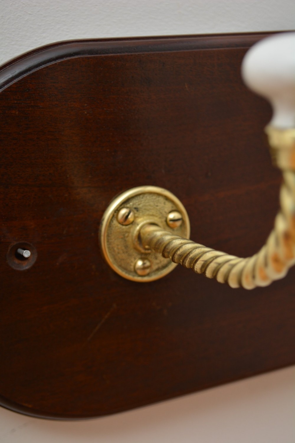 An oval mahogany wood backboard mounted with two twisted brass coat hooks featuring white ceramic end knobs. View VIII