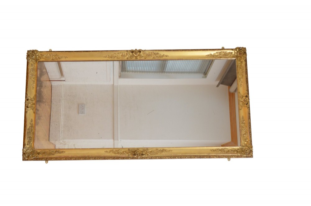 A tall rectangular floor-standing mirror with a gold-leaf gilded frame featuring intricate gesso moulding along the borders and corners. View III