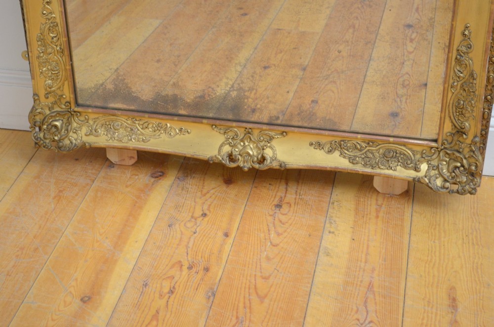A tall rectangular floor-standing mirror with a gold-leaf gilded frame featuring intricate gesso moulding along the borders and corners. View V