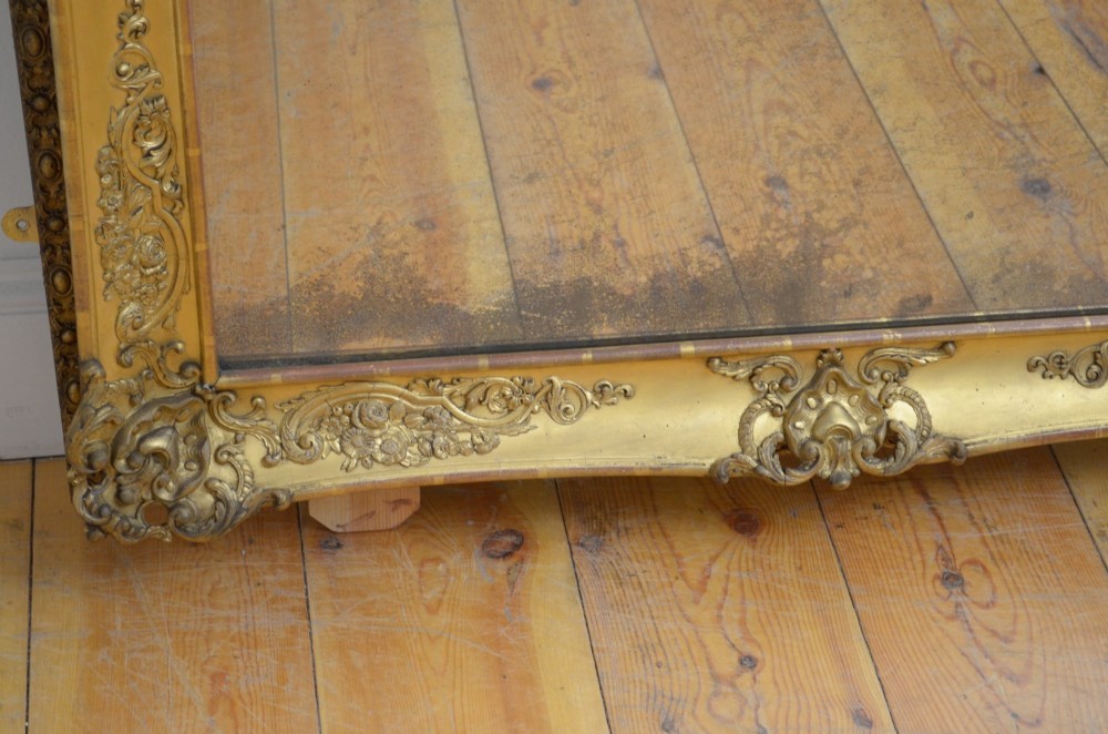 A tall rectangular floor-standing mirror with a gold-leaf gilded frame featuring intricate gesso moulding along the borders and corners. View VI