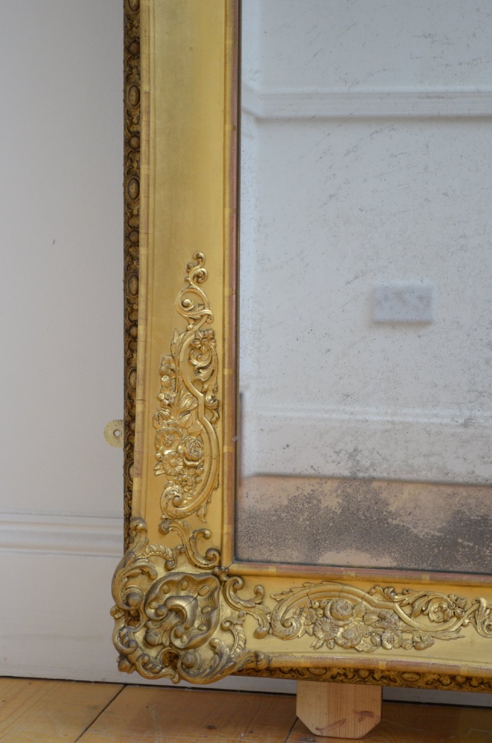 A tall rectangular floor-standing mirror with a gold-leaf gilded frame featuring intricate gesso moulding along the borders and corners. View VII