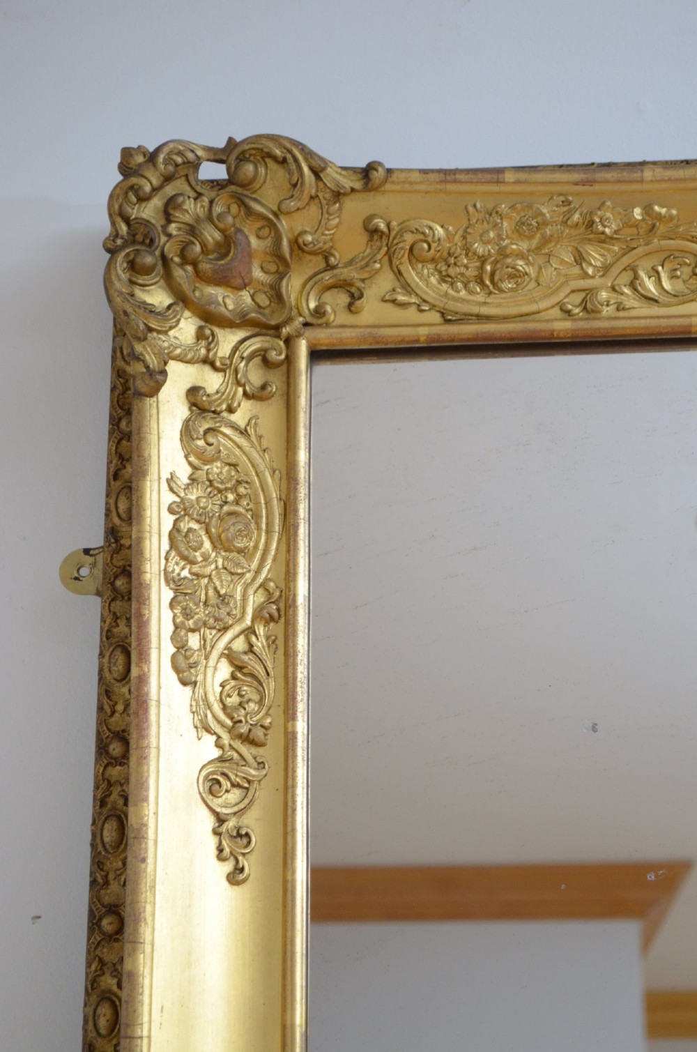 A tall rectangular floor-standing mirror with a gold-leaf gilded frame featuring intricate gesso moulding along the borders and corners. View IX
