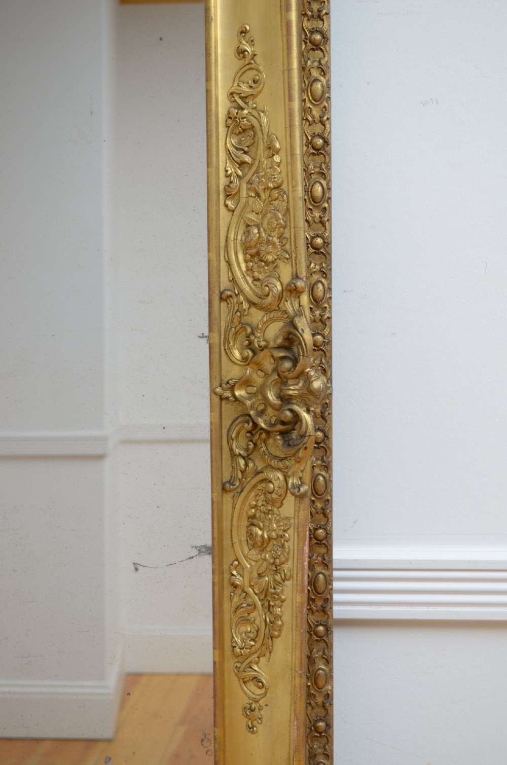 A tall rectangular floor-standing mirror with a gold-leaf gilded frame featuring intricate gesso moulding along the borders and corners. View XV