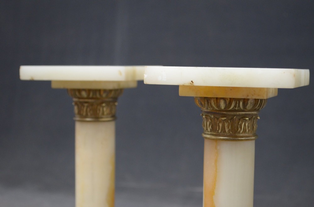 A pair of low Neoclassical onyx pedestal columns with square stepped bases, cylindrical stone shafts, and decorative brass capitals. View IX