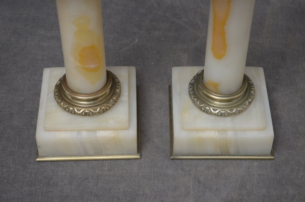 A pair of low Neoclassical onyx pedestal columns with square stepped bases, cylindrical stone shafts, and decorative brass capitals. View XII