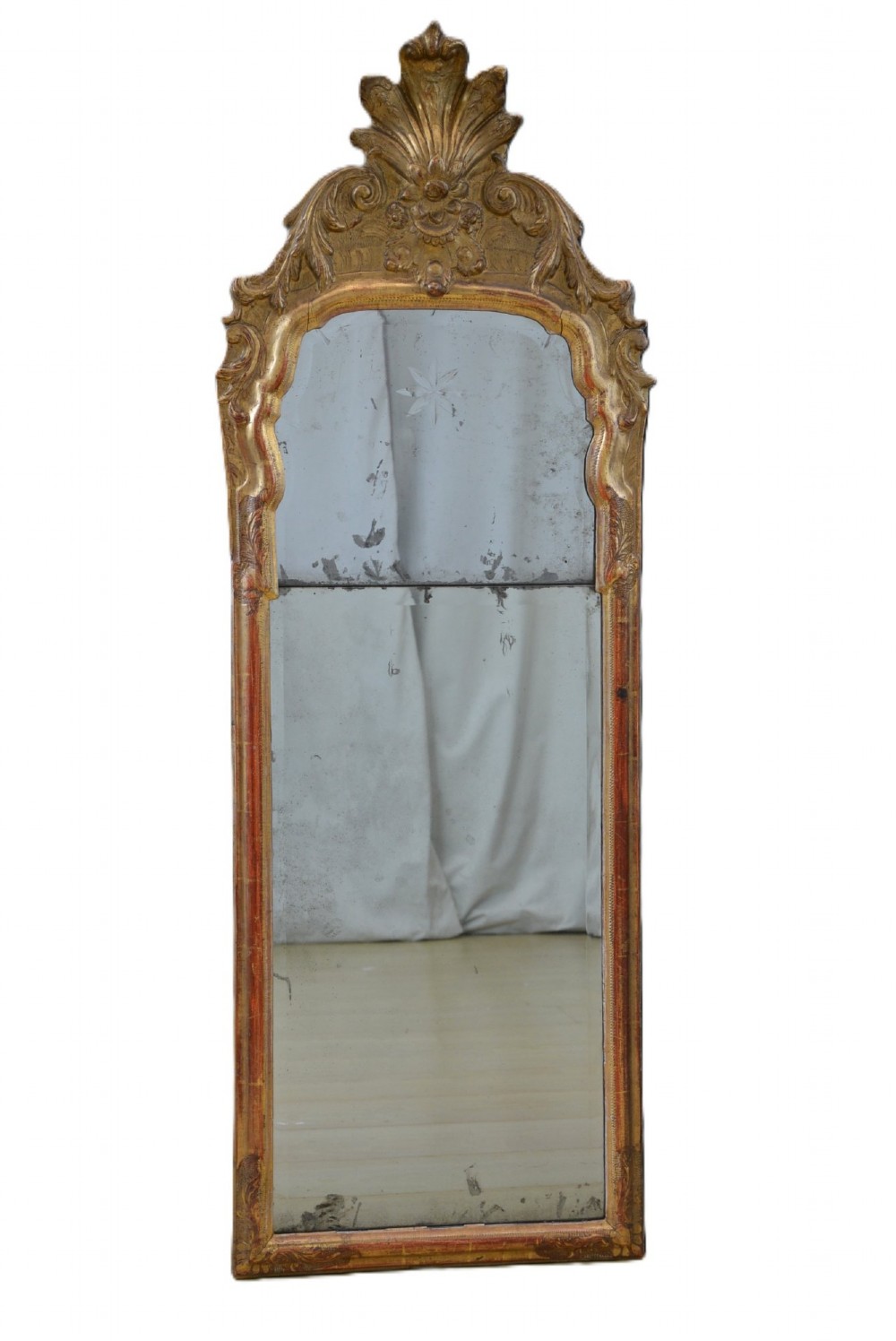 A tall, narrow Georgian giltwood pier mirror featuring a carved shell crest, scrollwork frame, and a split glass mirror plate.