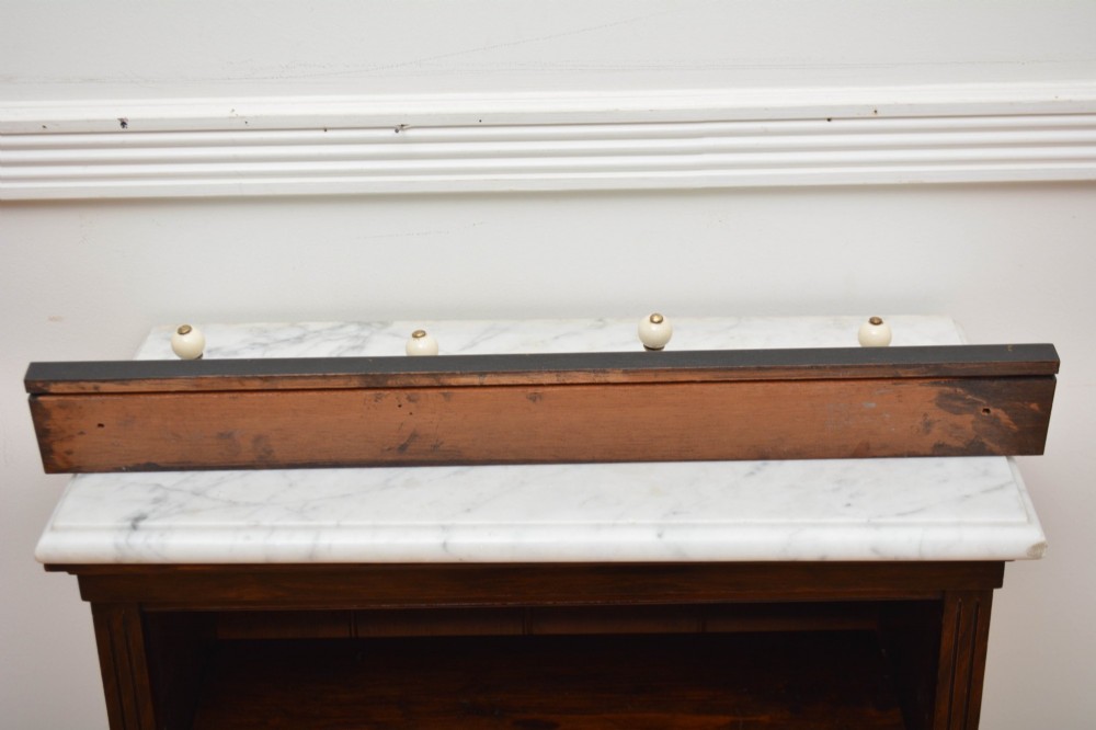 A pair of wall-mounted ebonised black wooden rails fitted with curved brass coat hooks ending in white ceramic knobs. View II