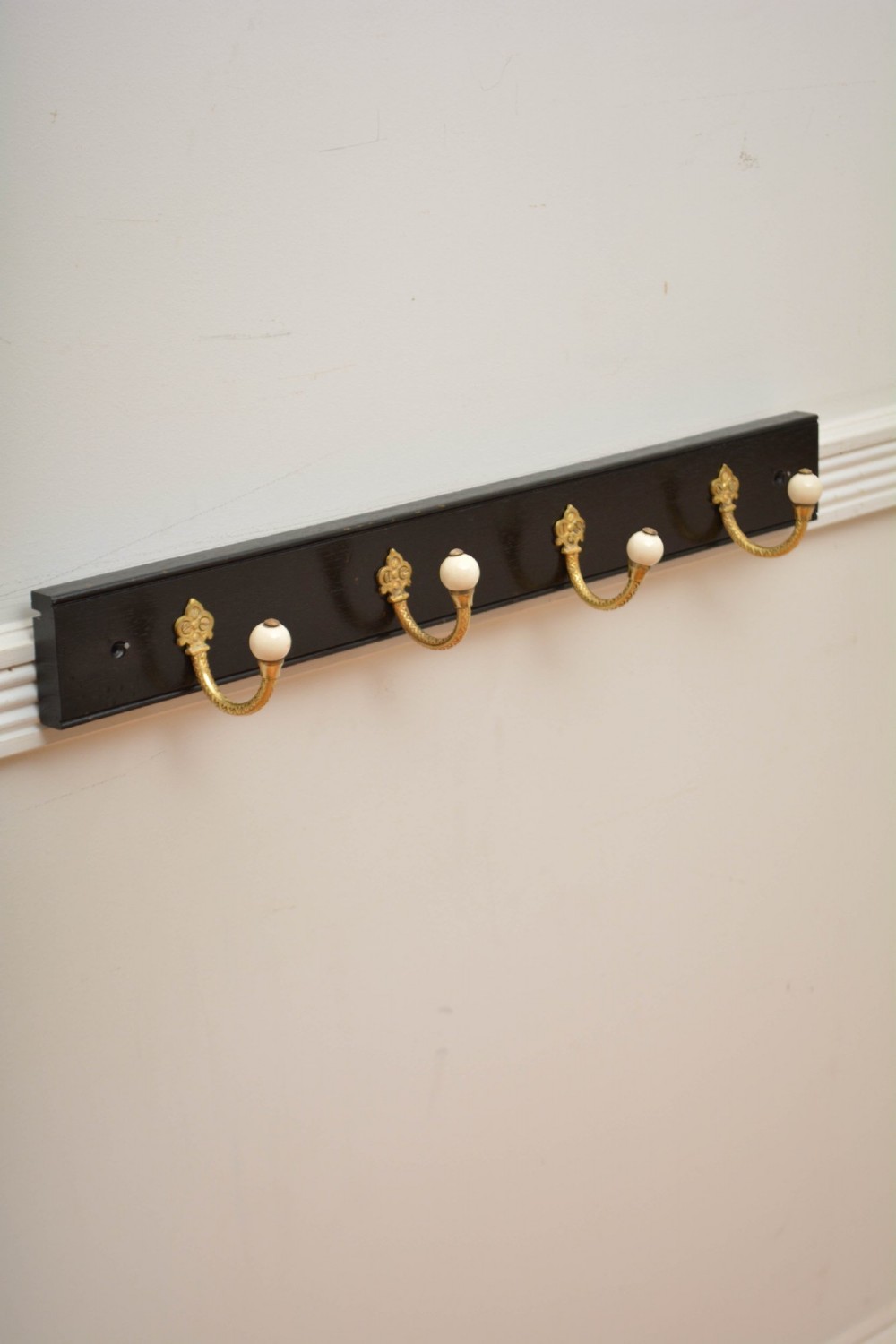 A pair of wall-mounted ebonised black wooden rails fitted with curved brass coat hooks ending in white ceramic knobs. View III