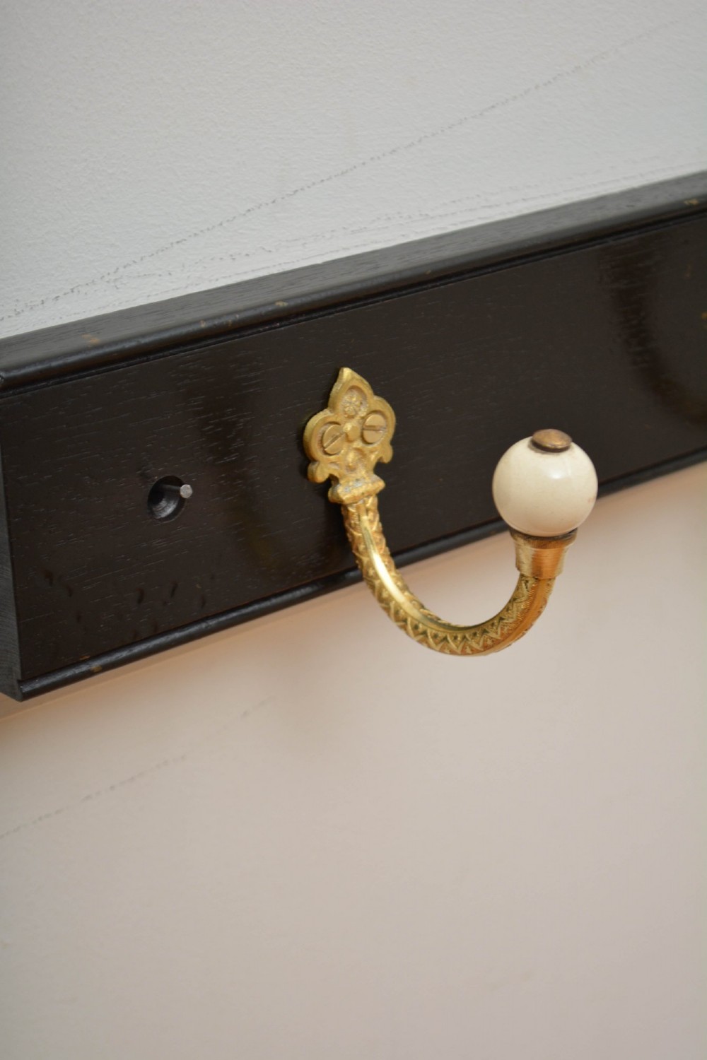 A pair of wall-mounted ebonised black wooden rails fitted with curved brass coat hooks ending in white ceramic knobs. View V