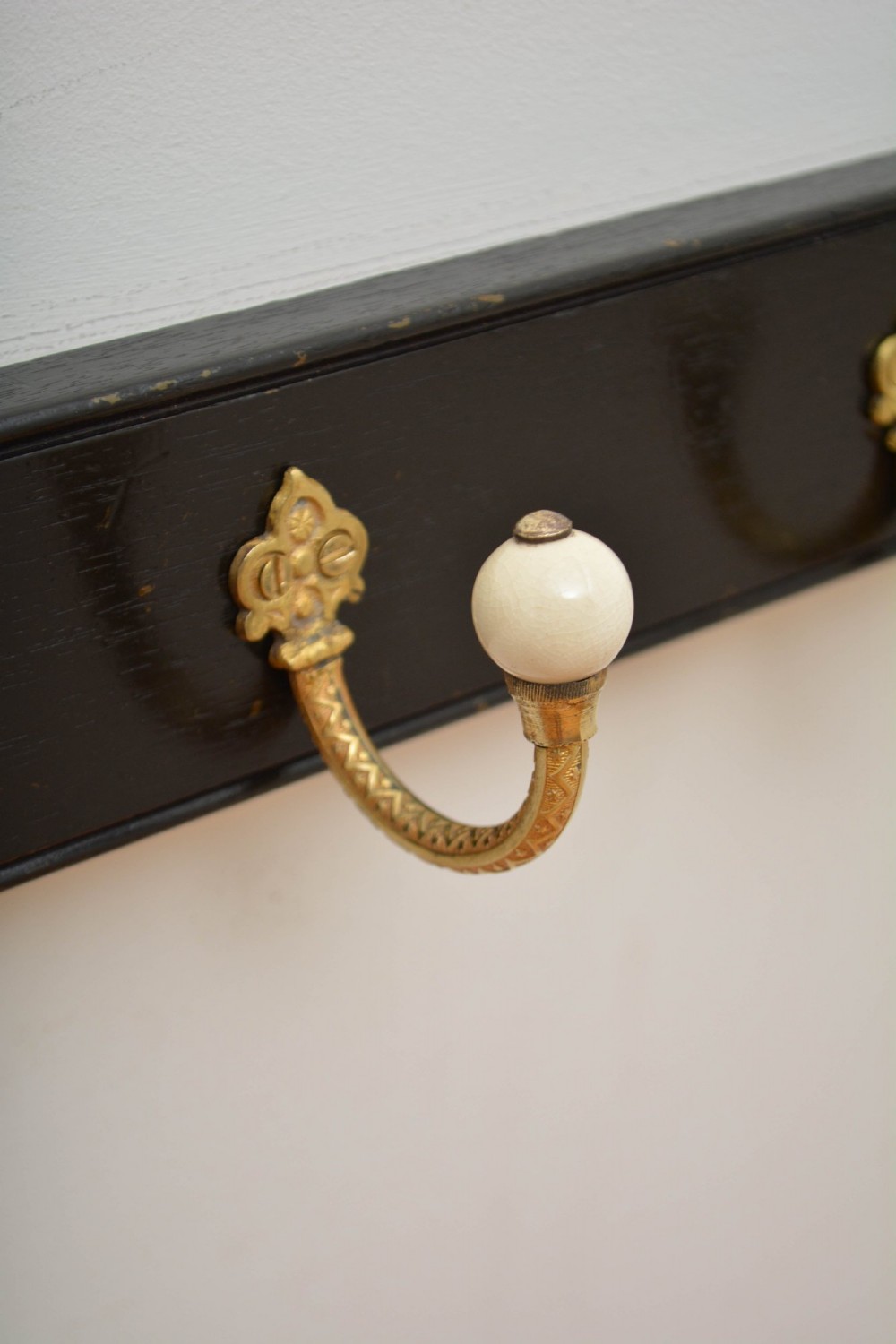 A pair of wall-mounted ebonised black wooden rails fitted with curved brass coat hooks ending in white ceramic knobs. View VI