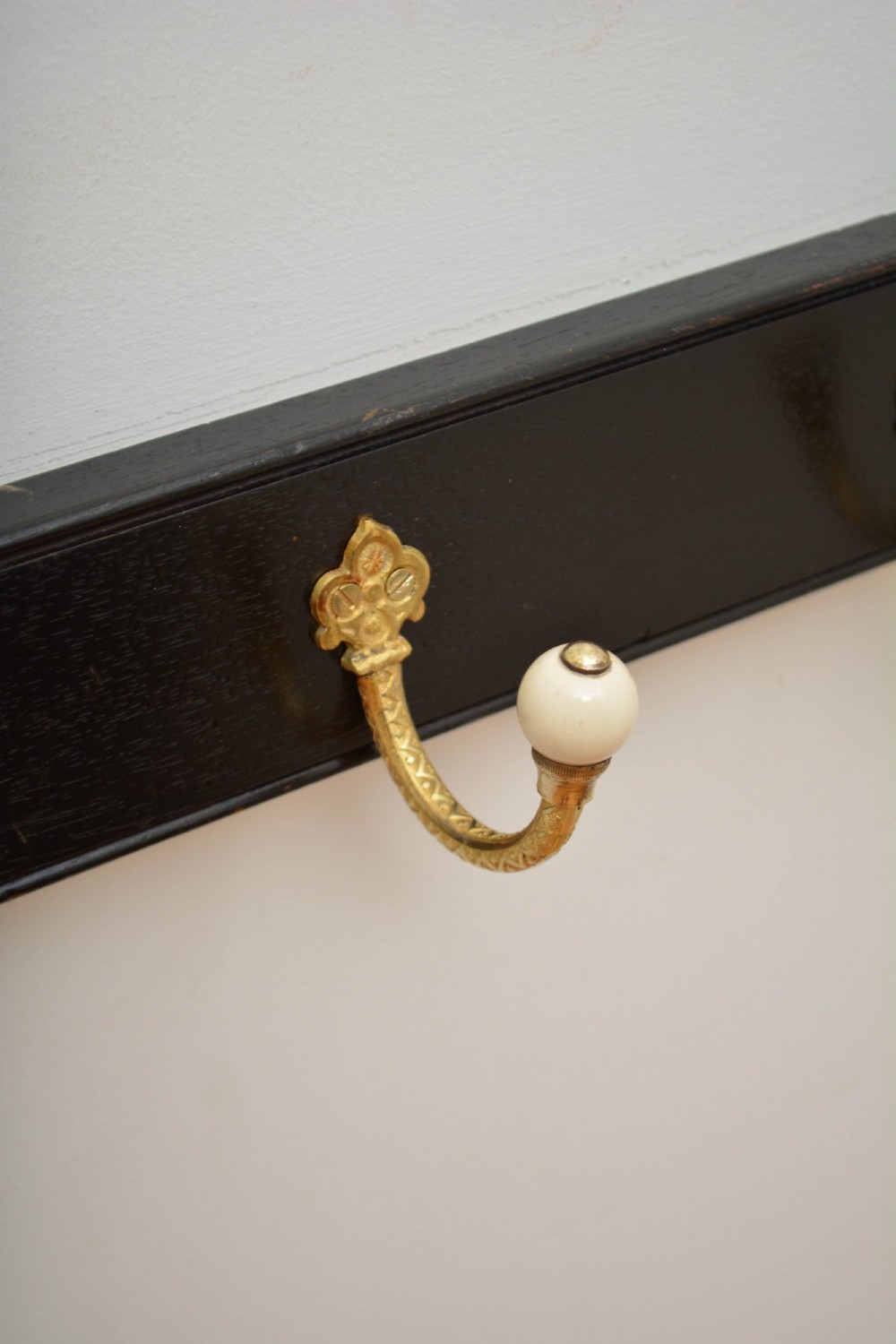 A pair of wall-mounted ebonised black wooden rails fitted with curved brass coat hooks ending in white ceramic knobs. View IX