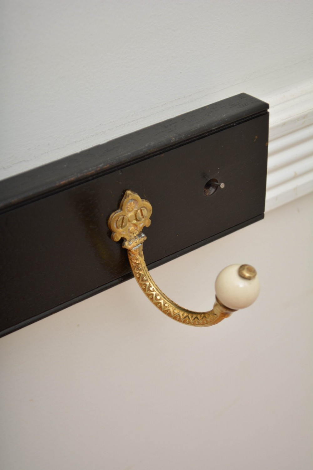 A pair of wall-mounted ebonised black wooden rails fitted with curved brass coat hooks ending in white ceramic knobs. View X
