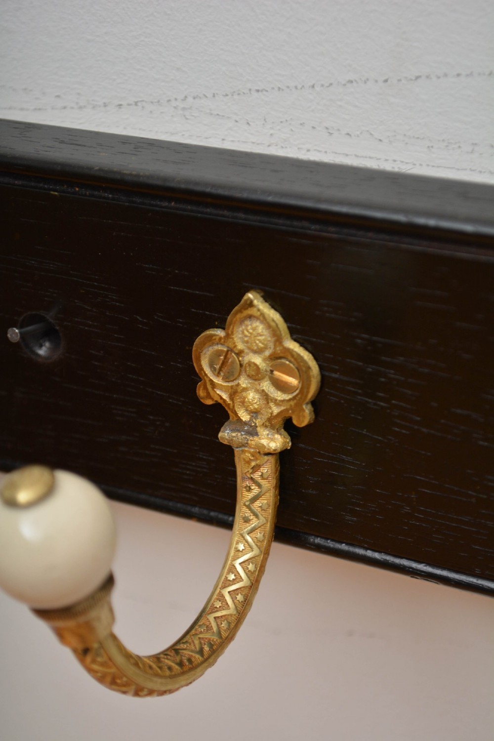 A pair of wall-mounted ebonised black wooden rails fitted with curved brass coat hooks ending in white ceramic knobs. View XI