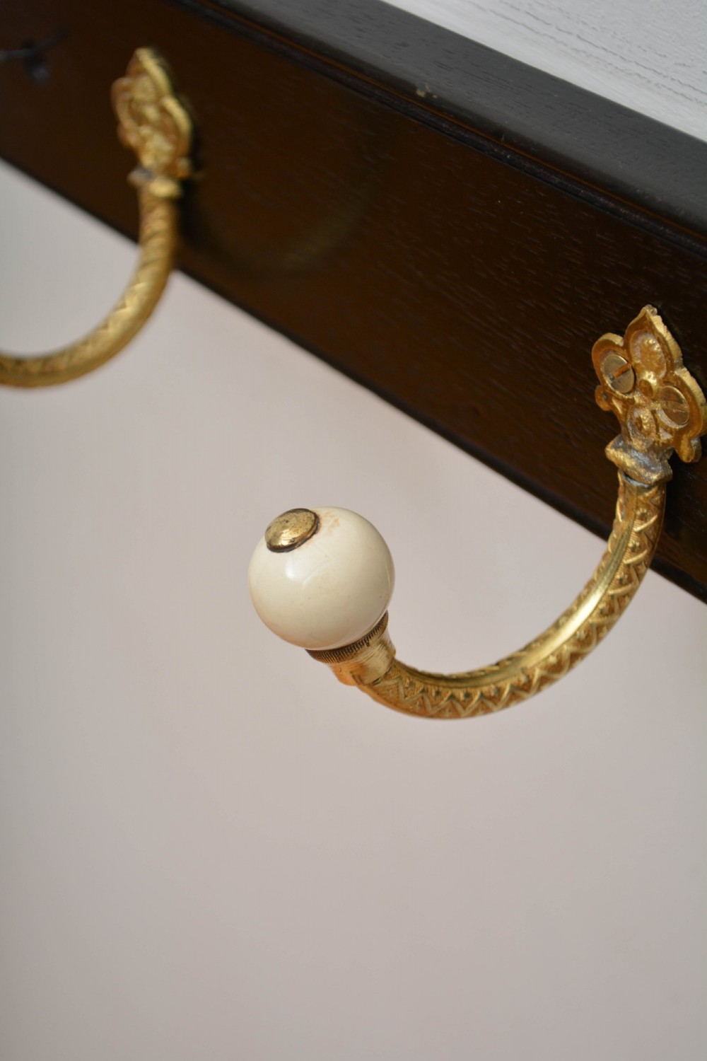 A pair of wall-mounted ebonised black wooden rails fitted with curved brass coat hooks ending in white ceramic knobs. View XIII