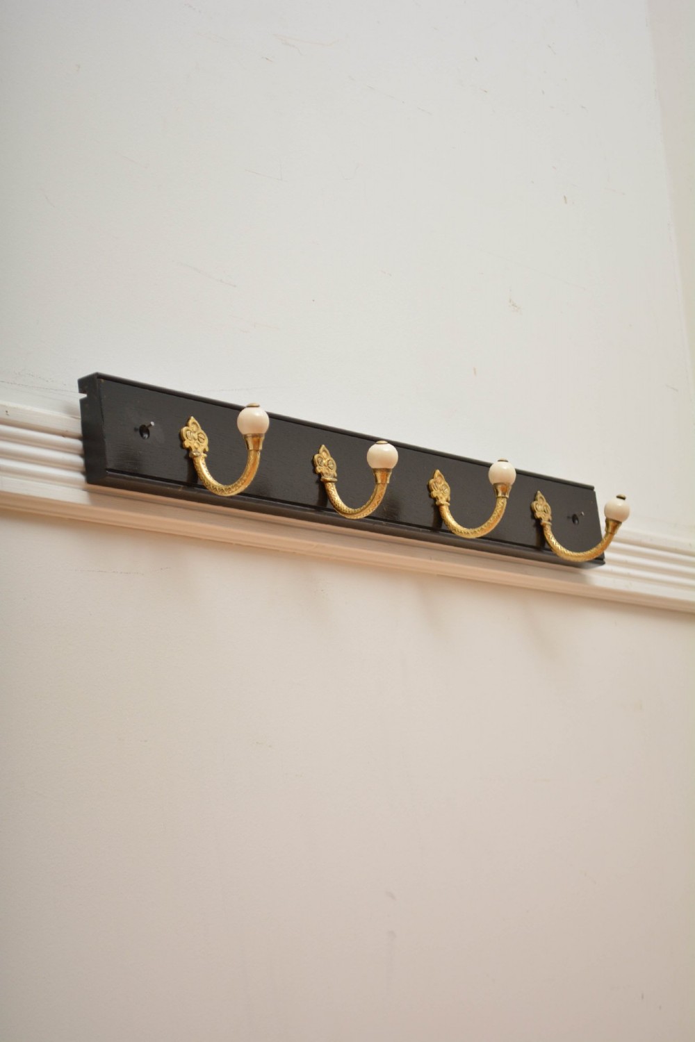 A pair of wall-mounted ebonised black wooden rails fitted with curved brass coat hooks ending in white ceramic knobs. View XIV