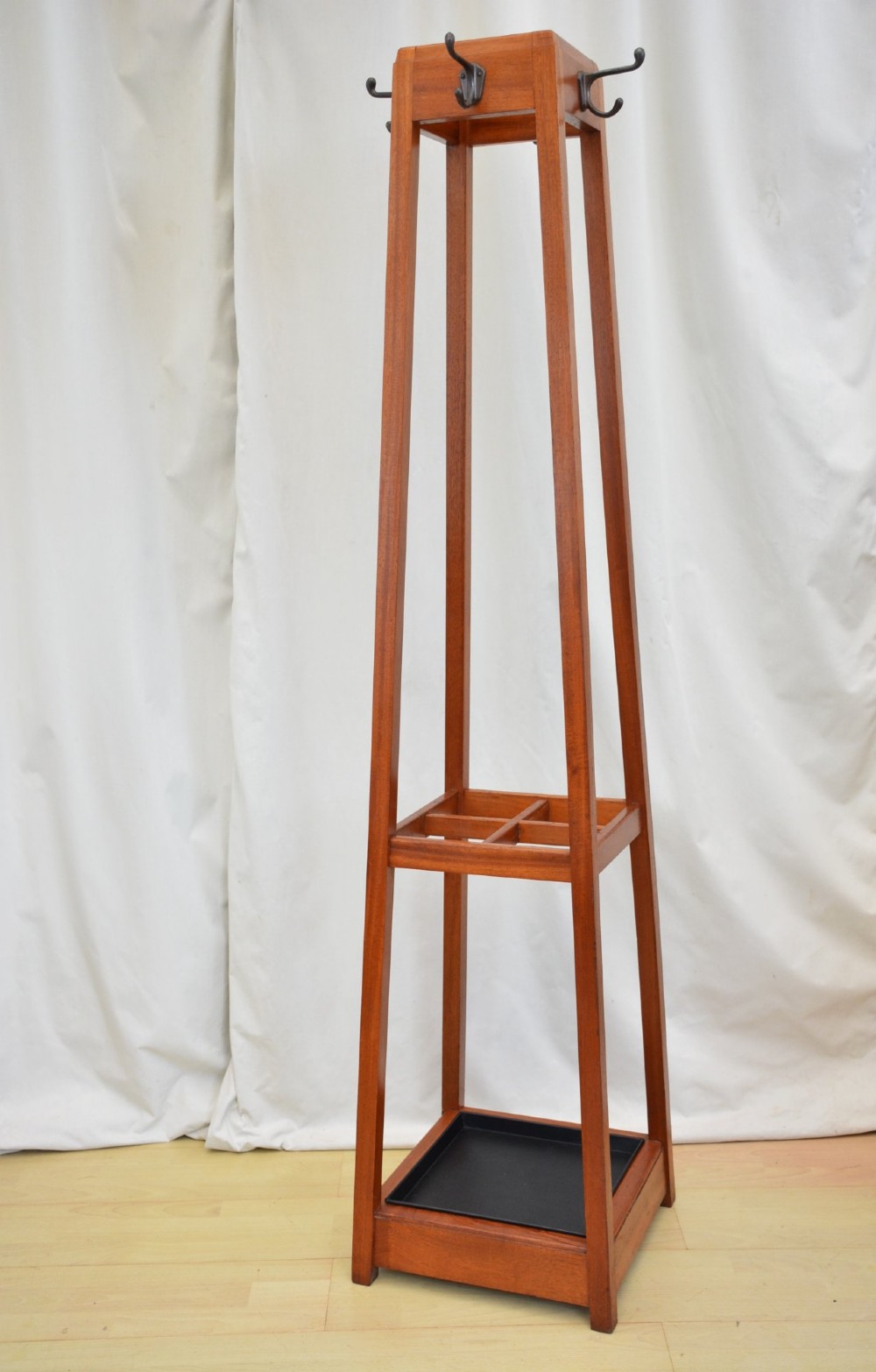 A tall, square-framed Art Deco wooden coat stand with dark metal hanging hooks and a lower umbrella drip tray. View II