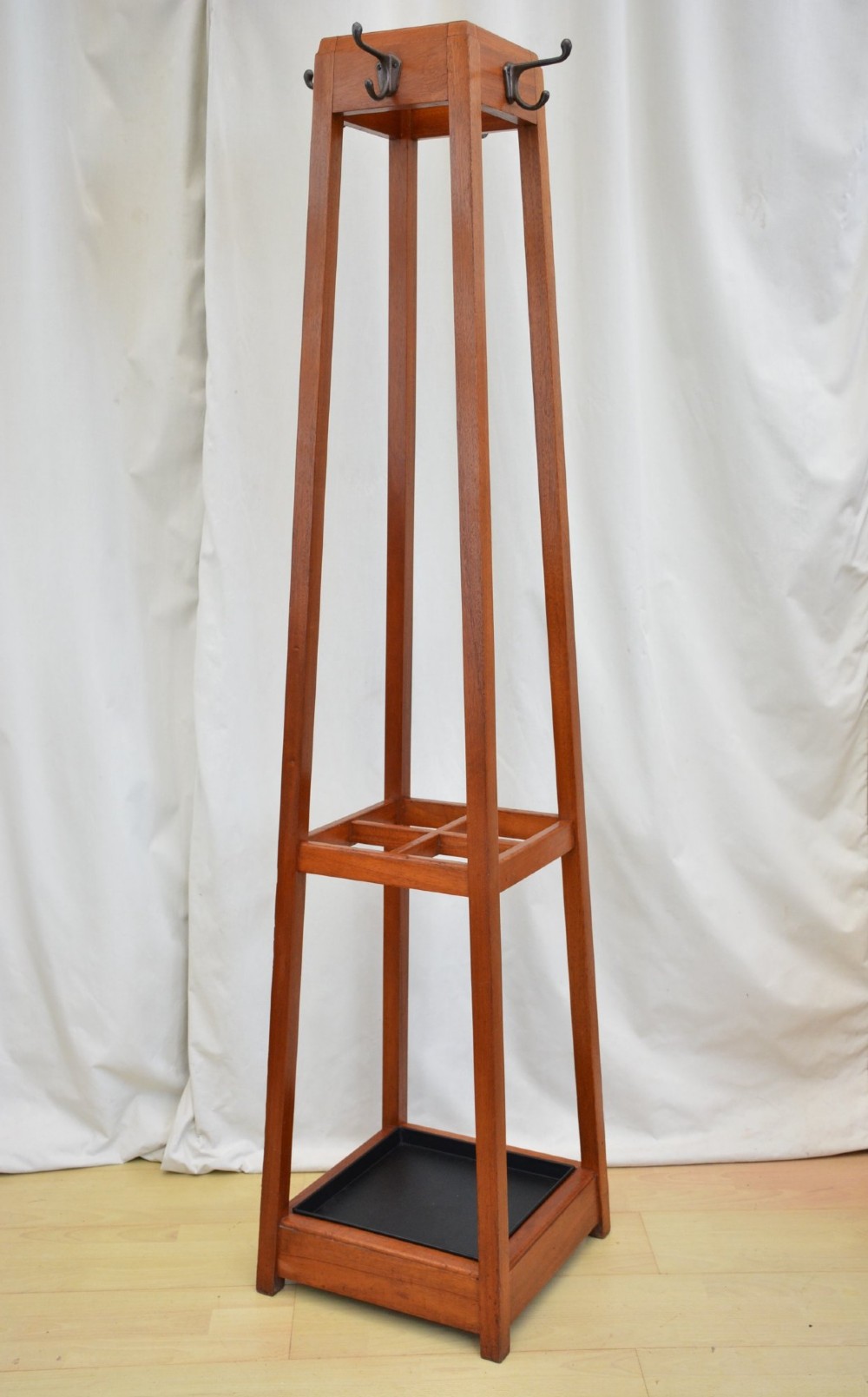 A tall, square-framed Art Deco wooden coat stand with dark metal hanging hooks and a lower umbrella drip tray. View III