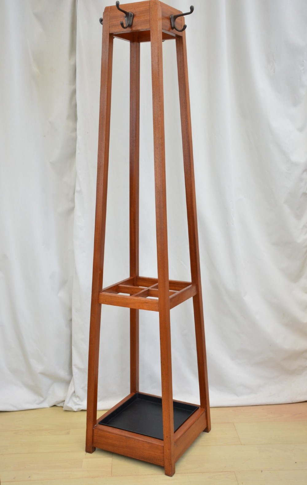 A tall, square-framed Art Deco wooden coat stand with dark metal hanging hooks and a lower umbrella drip tray. View IV