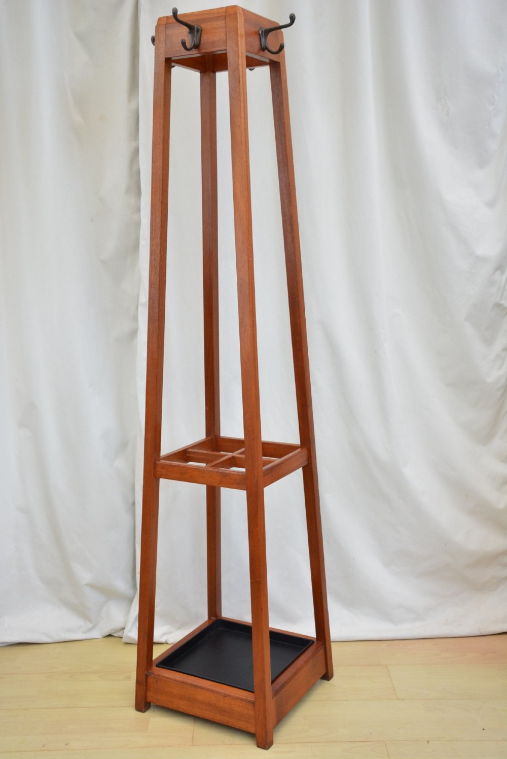 A tall, square-framed Art Deco wooden coat stand with dark metal hanging hooks and a lower umbrella drip tray. View V