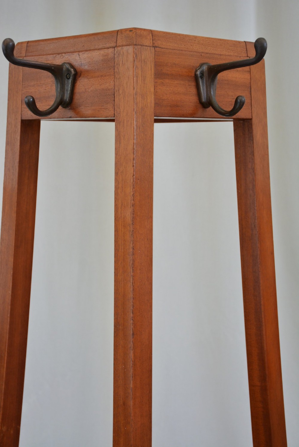 A tall, square-framed Art Deco wooden coat stand with dark metal hanging hooks and a lower umbrella drip tray. View VI