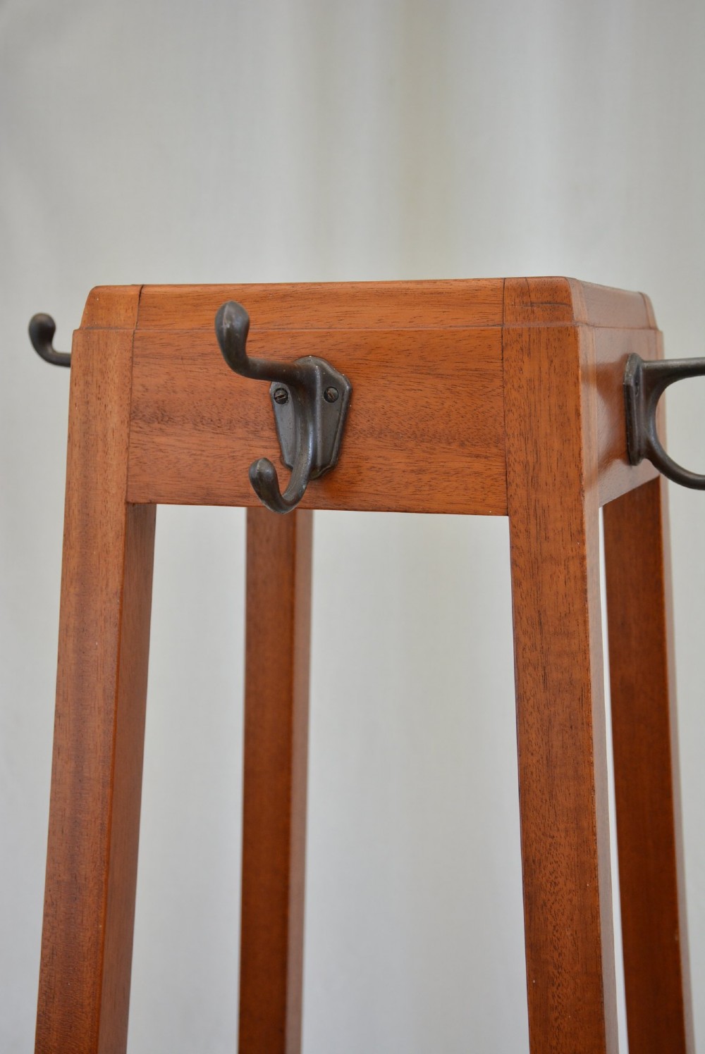 A tall, square-framed Art Deco wooden coat stand with dark metal hanging hooks and a lower umbrella drip tray. View VII