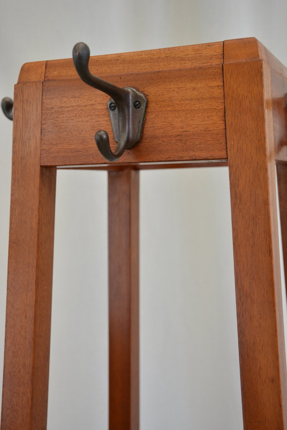 A tall, square-framed Art Deco wooden coat stand with dark metal hanging hooks and a lower umbrella drip tray. View IX